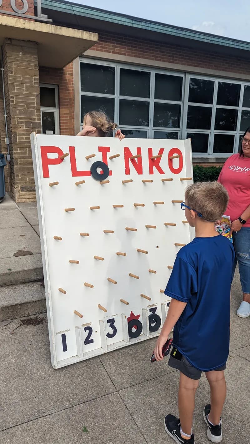 A student, seen from behind, plays a Plinko game outside the school.